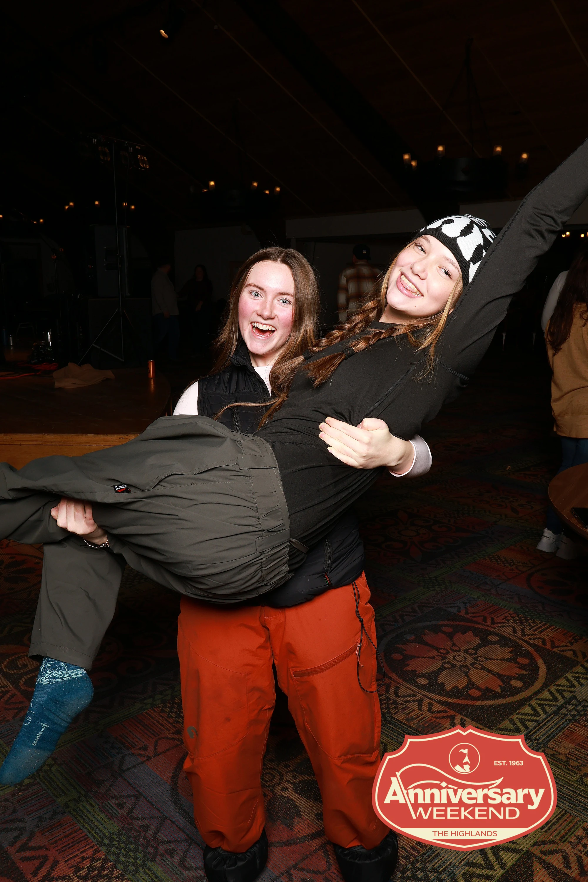 One friend carrying another across the frame at The Highlands Anniversary Weekend