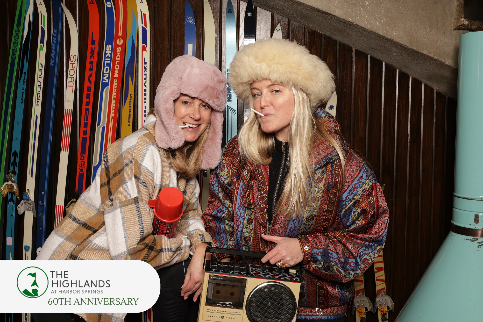 Two women in fur hats and vintage ski wear holding the boombox at The Highlands Anniversary Weekend