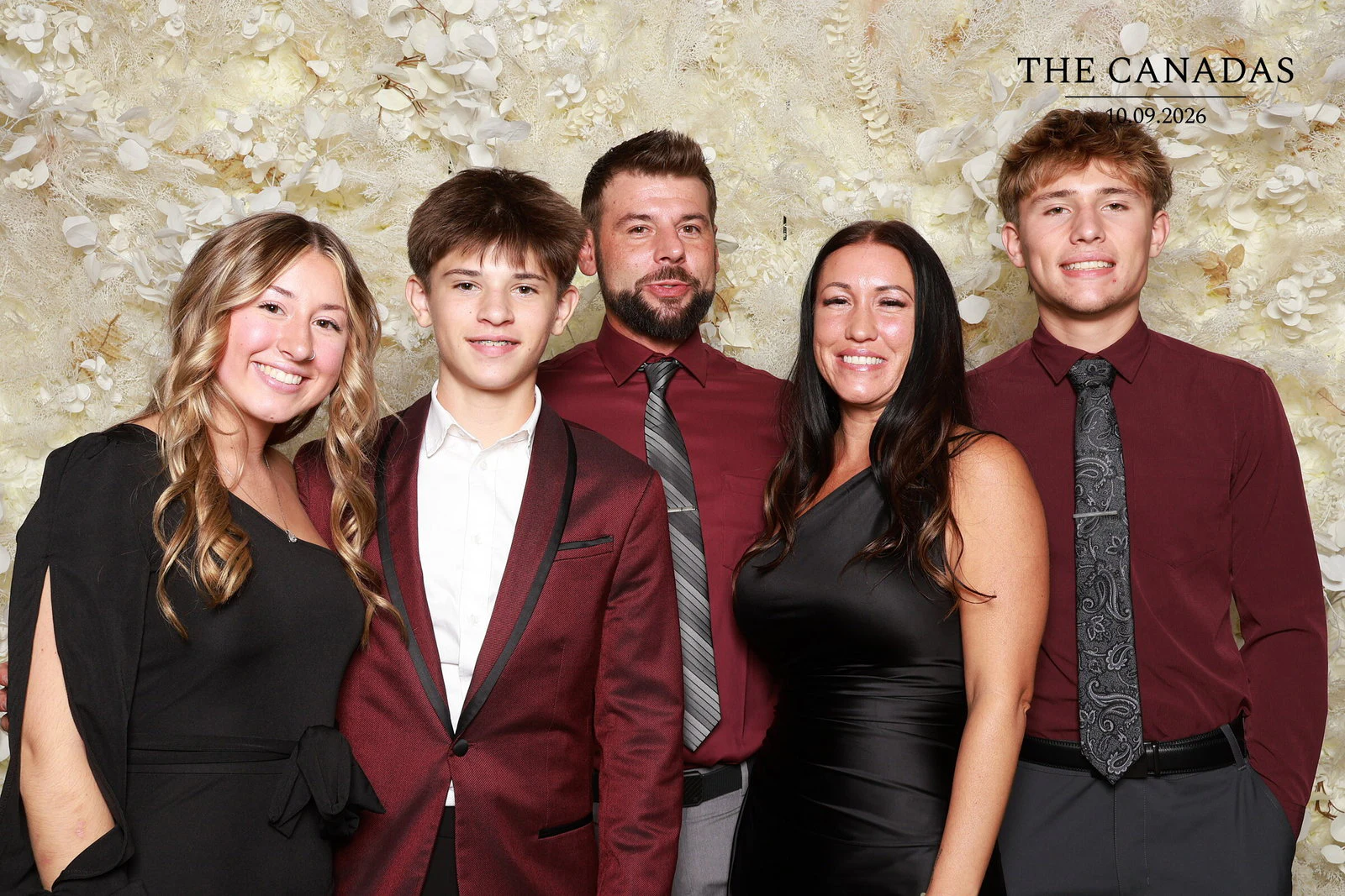 Five guests in black and burgundy standing close together, everyone smiling at Tristin + Emma