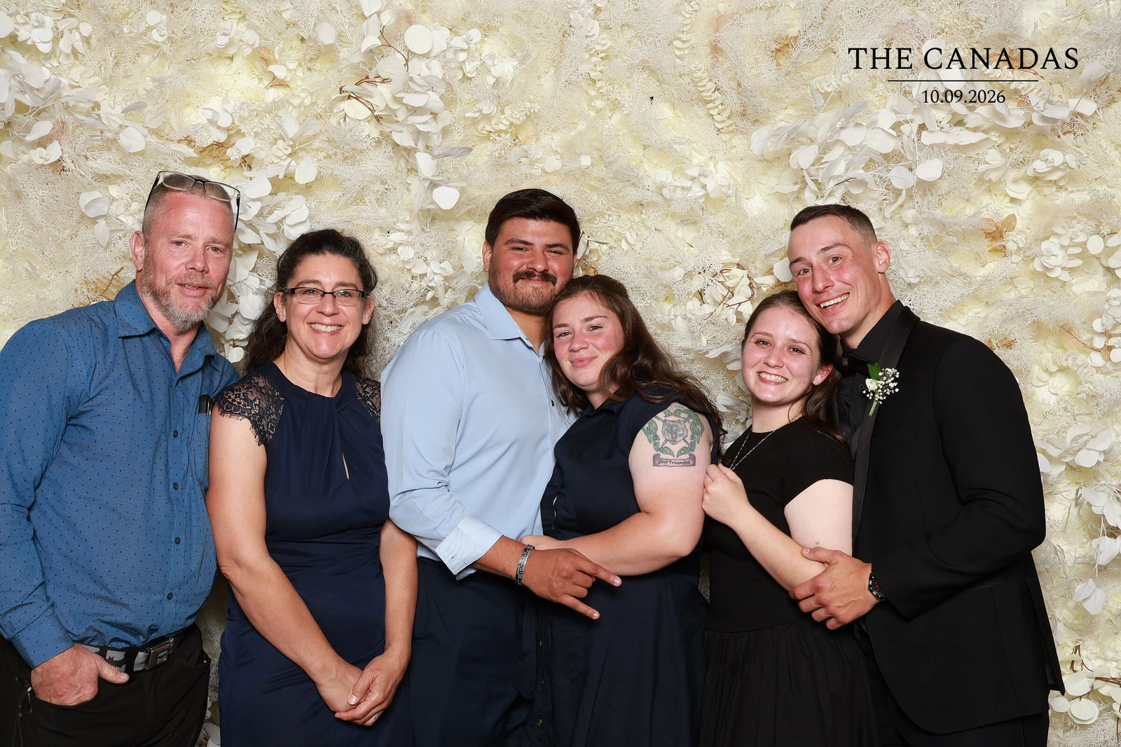 Six guests in a row with their arms around each other, everyone smiling at Tristin + Emma