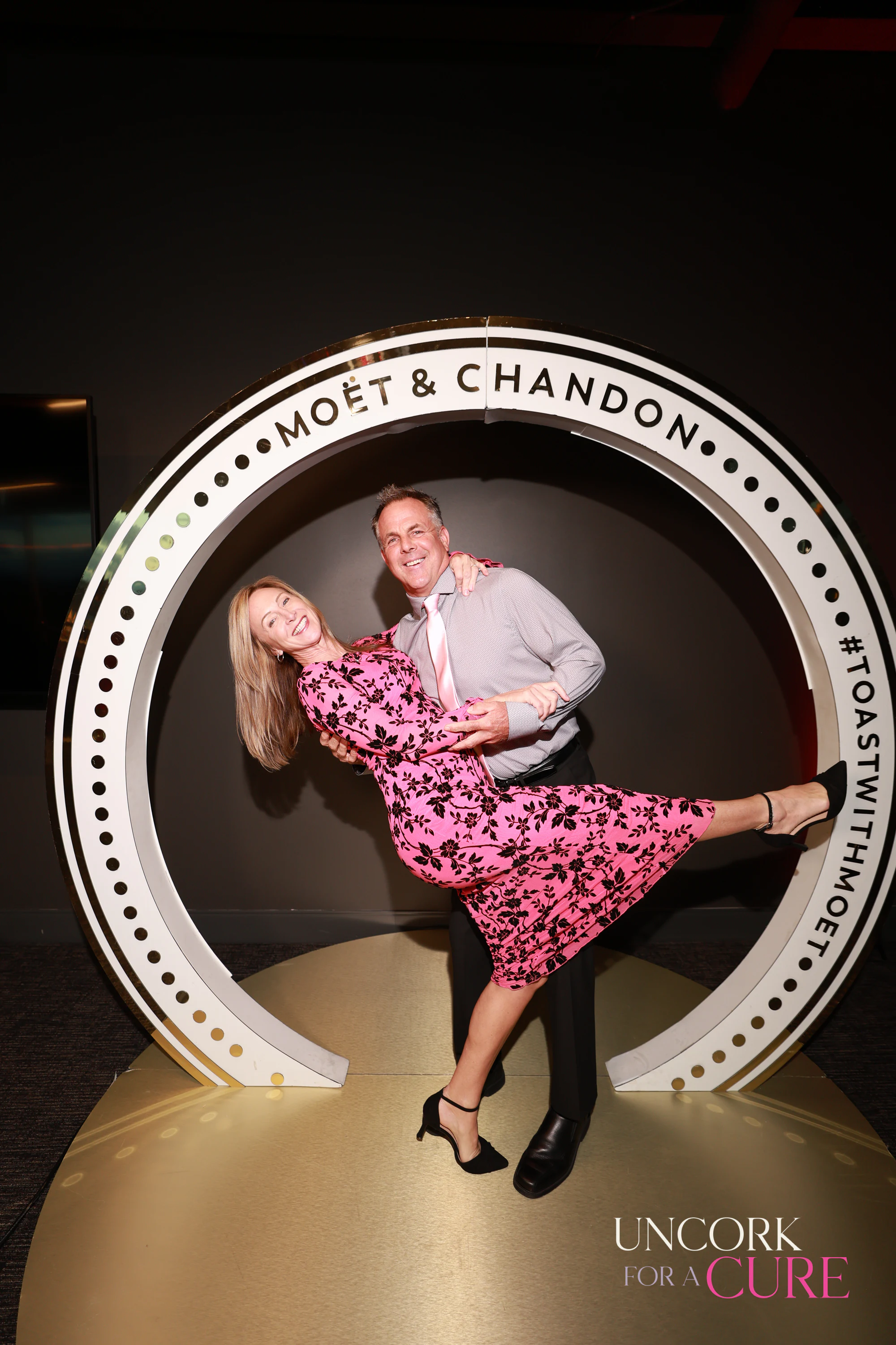 The couple laughing, her leg still up, in the Moët & Chandon ring at Uncork for a Cure 2026