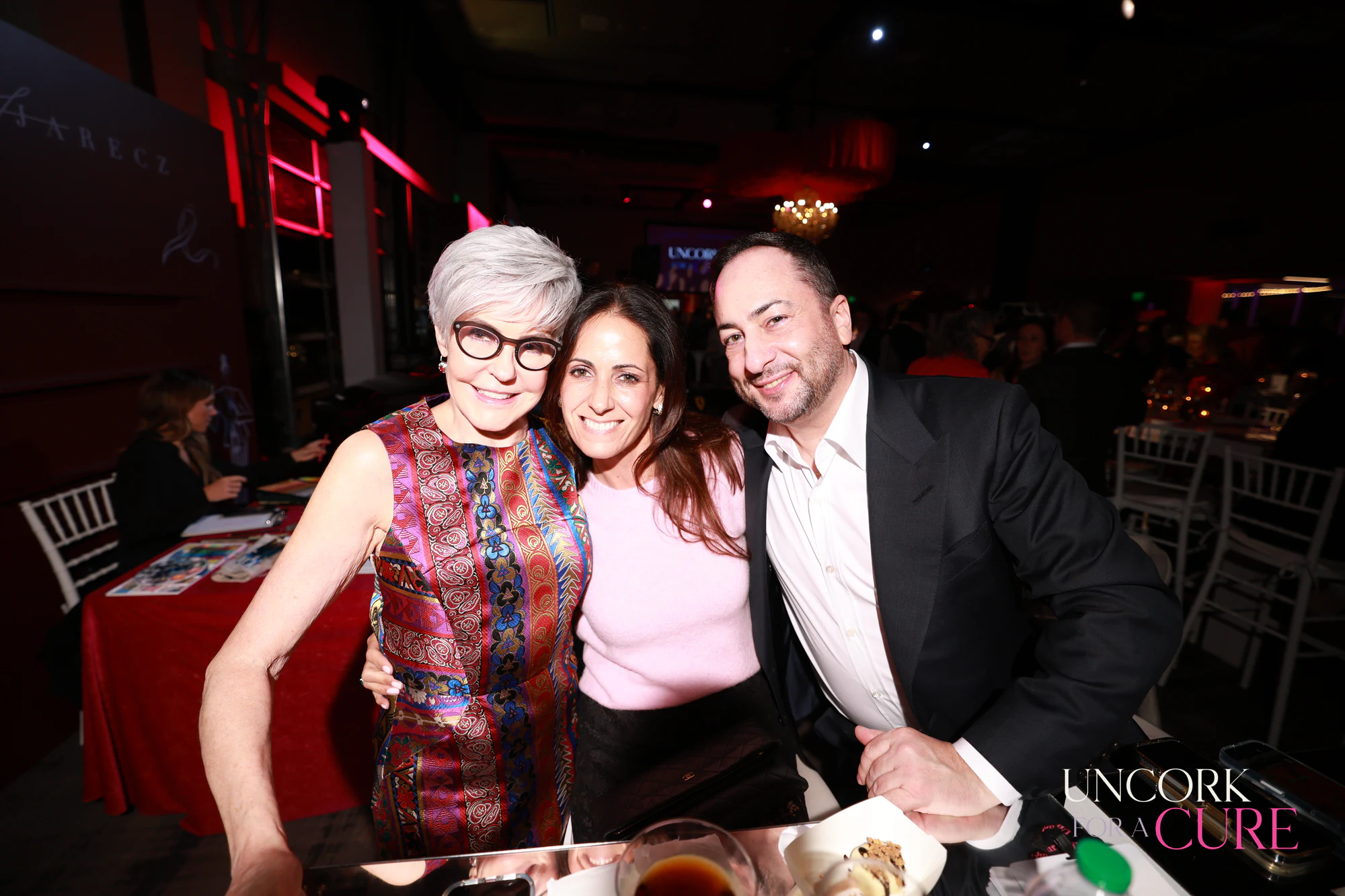 Three guests leaning in together at their table at Uncork for a Cure 2026