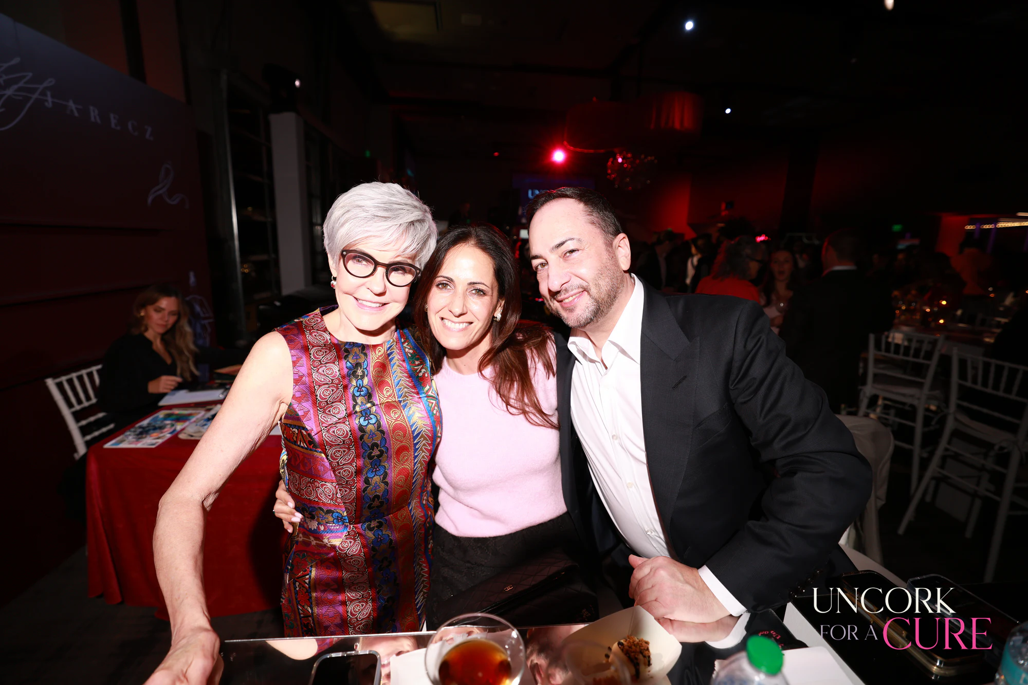 The three guests at their table, smiling wide at Uncork for a Cure 2026