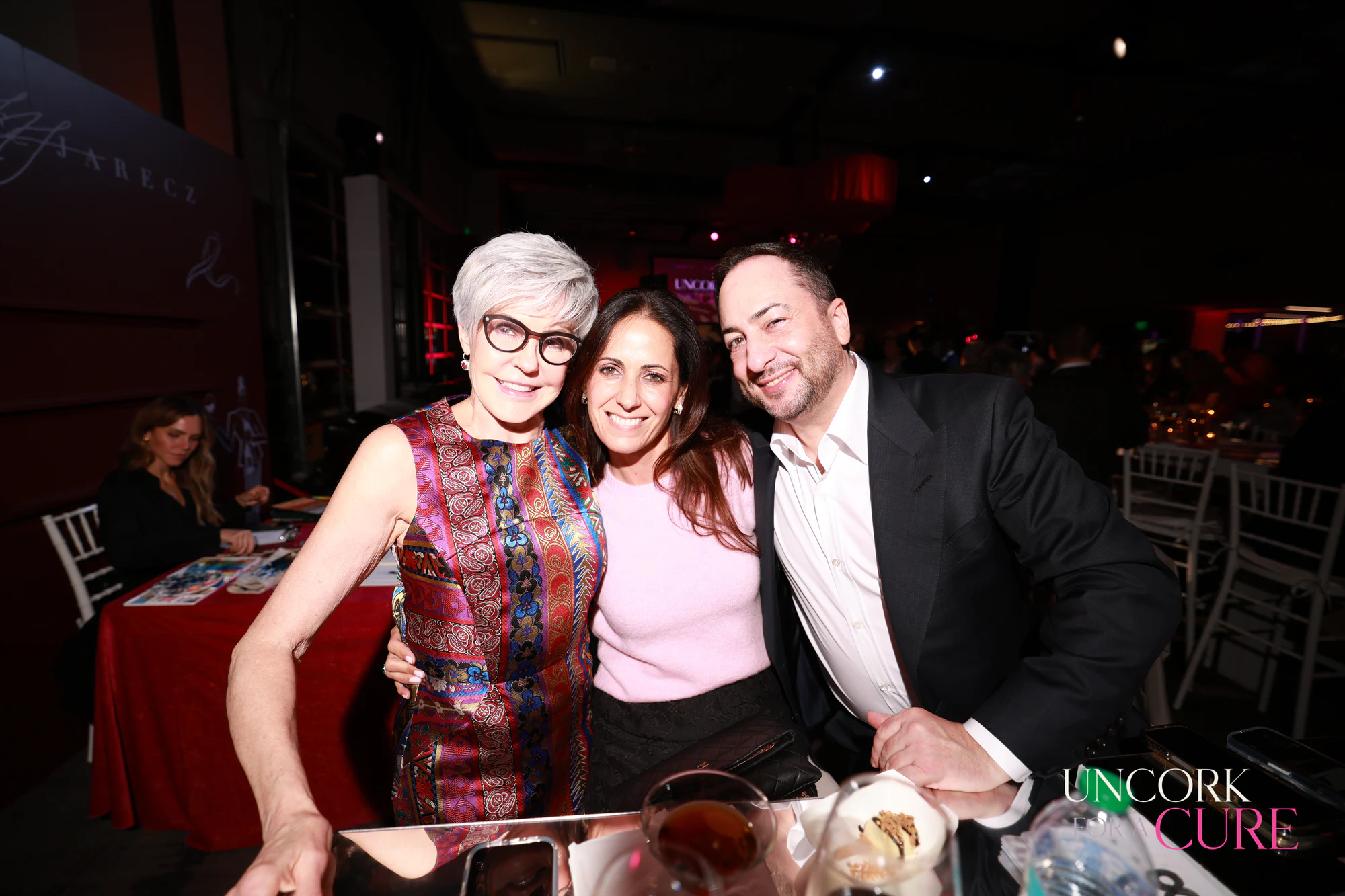 The three guests at their table, cheek to cheek at Uncork for a Cure 2026