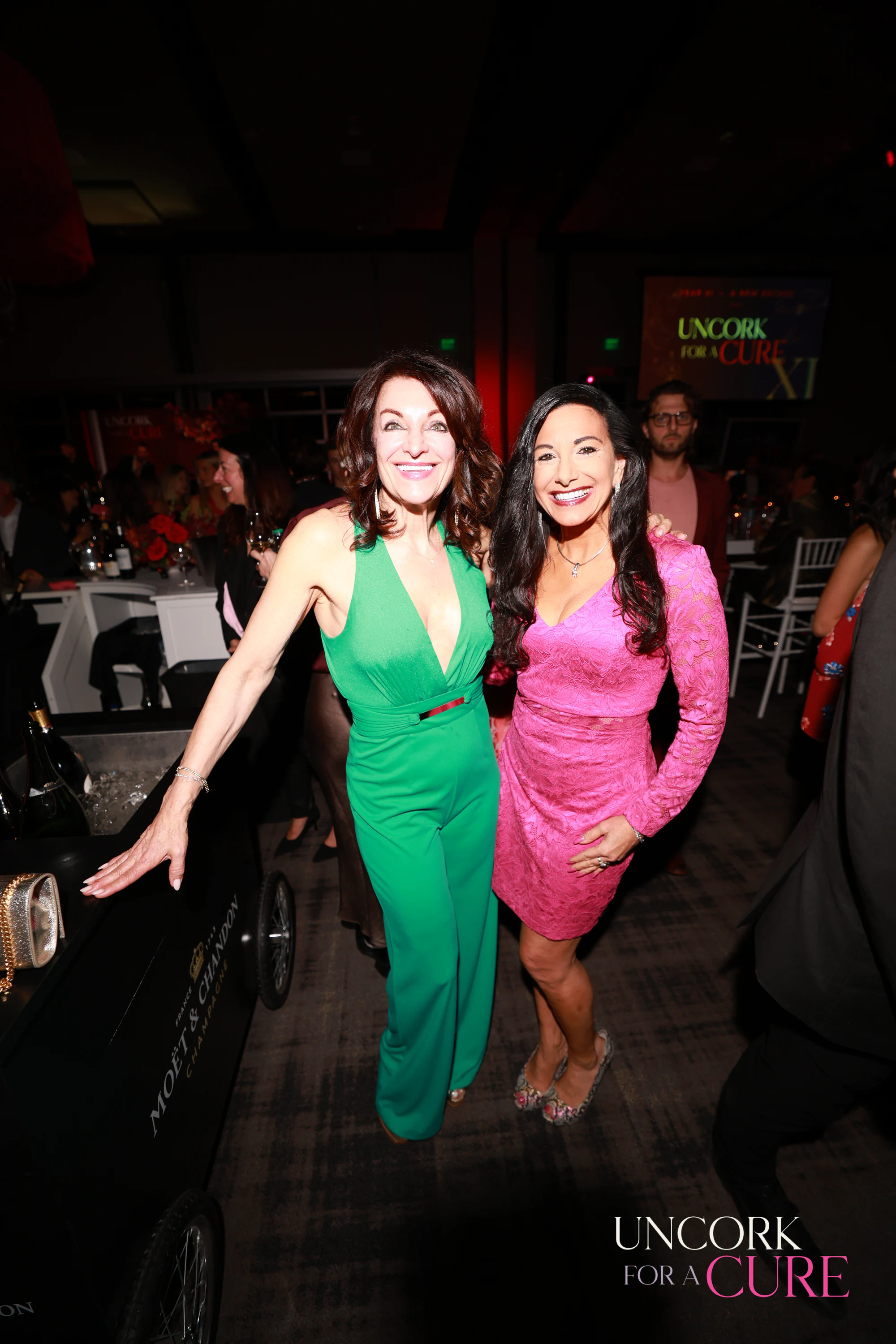 The two women in green and pink laughing at Uncork for a Cure 2026