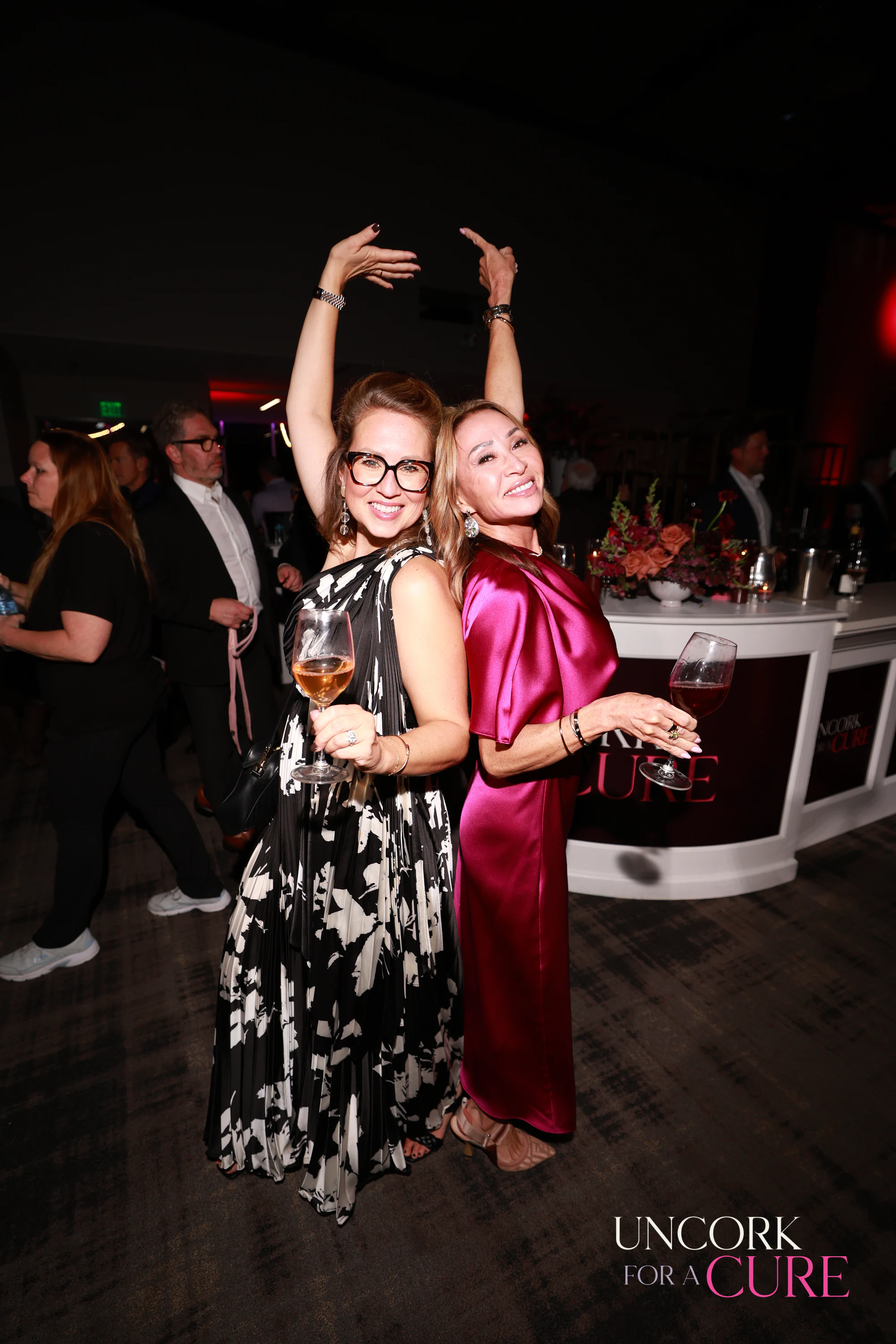 The two women dancing, glass in hand at Uncork for a Cure 2026