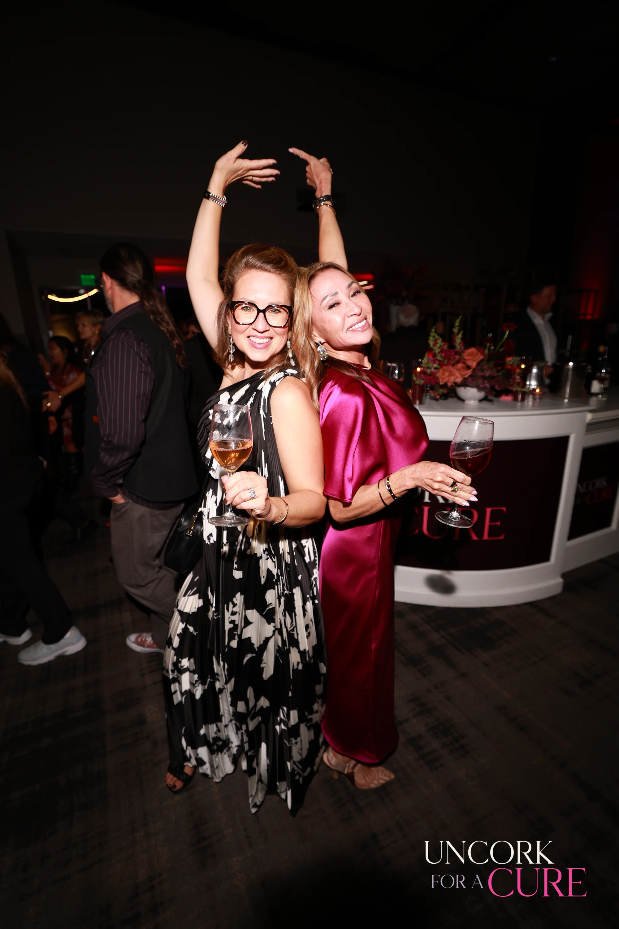 The two women posing, one arm still up at Uncork for a Cure 2026