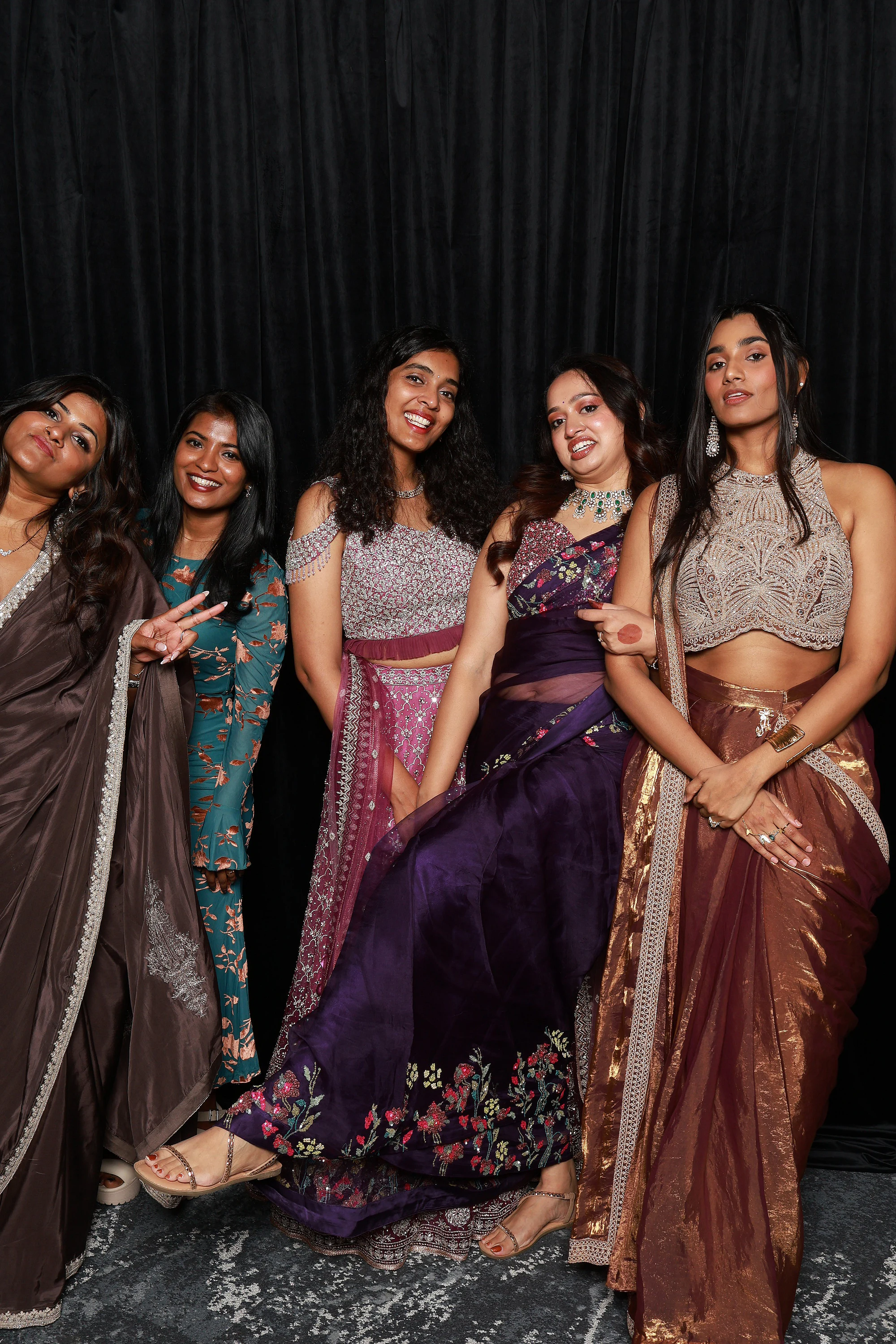 Five women posed together, seated and standing, saris and jewel tones at Yamini + Hari