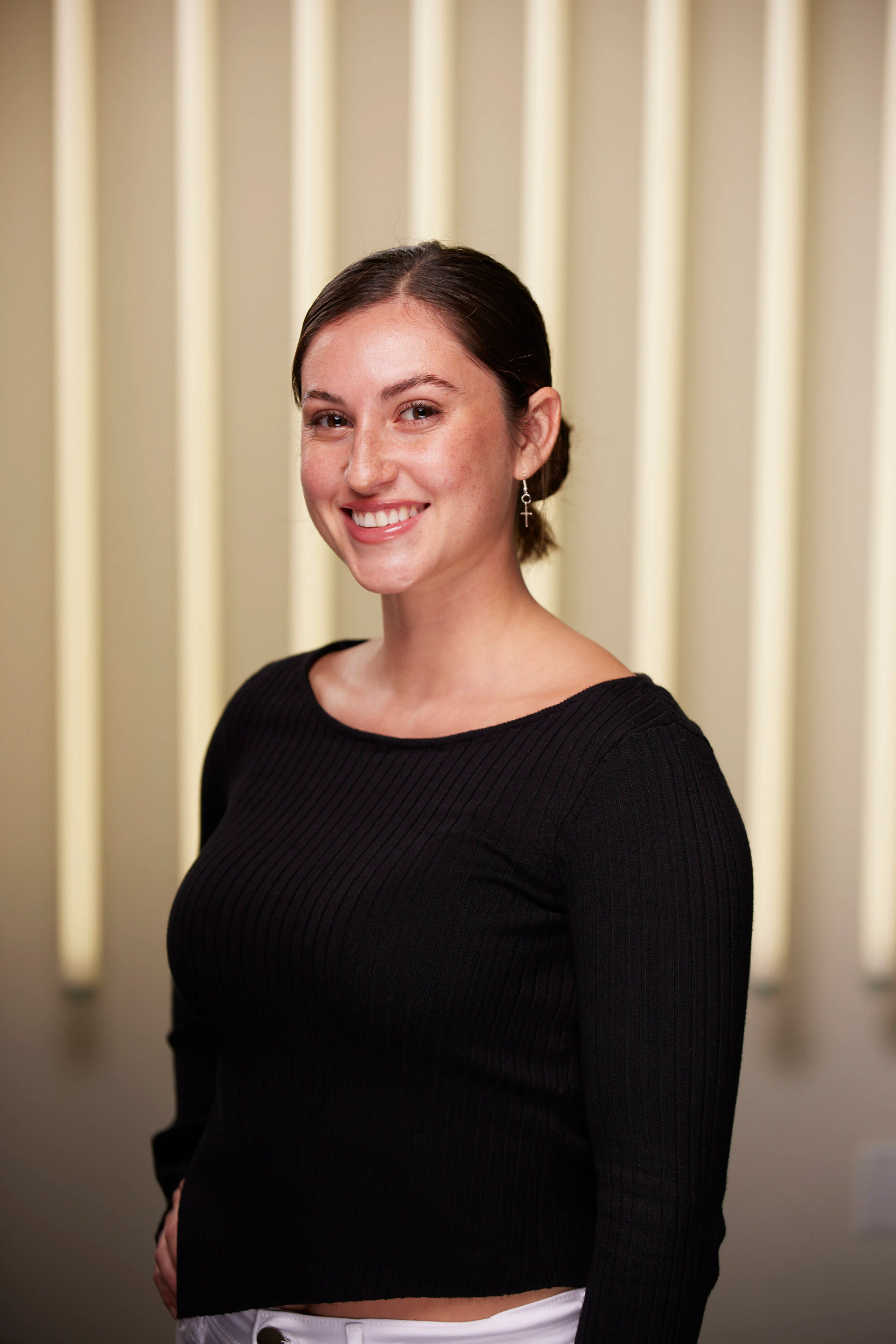 Black ribbed top, hair pulled back, smiling in front of the lit panel wall at Michigan Tech Week