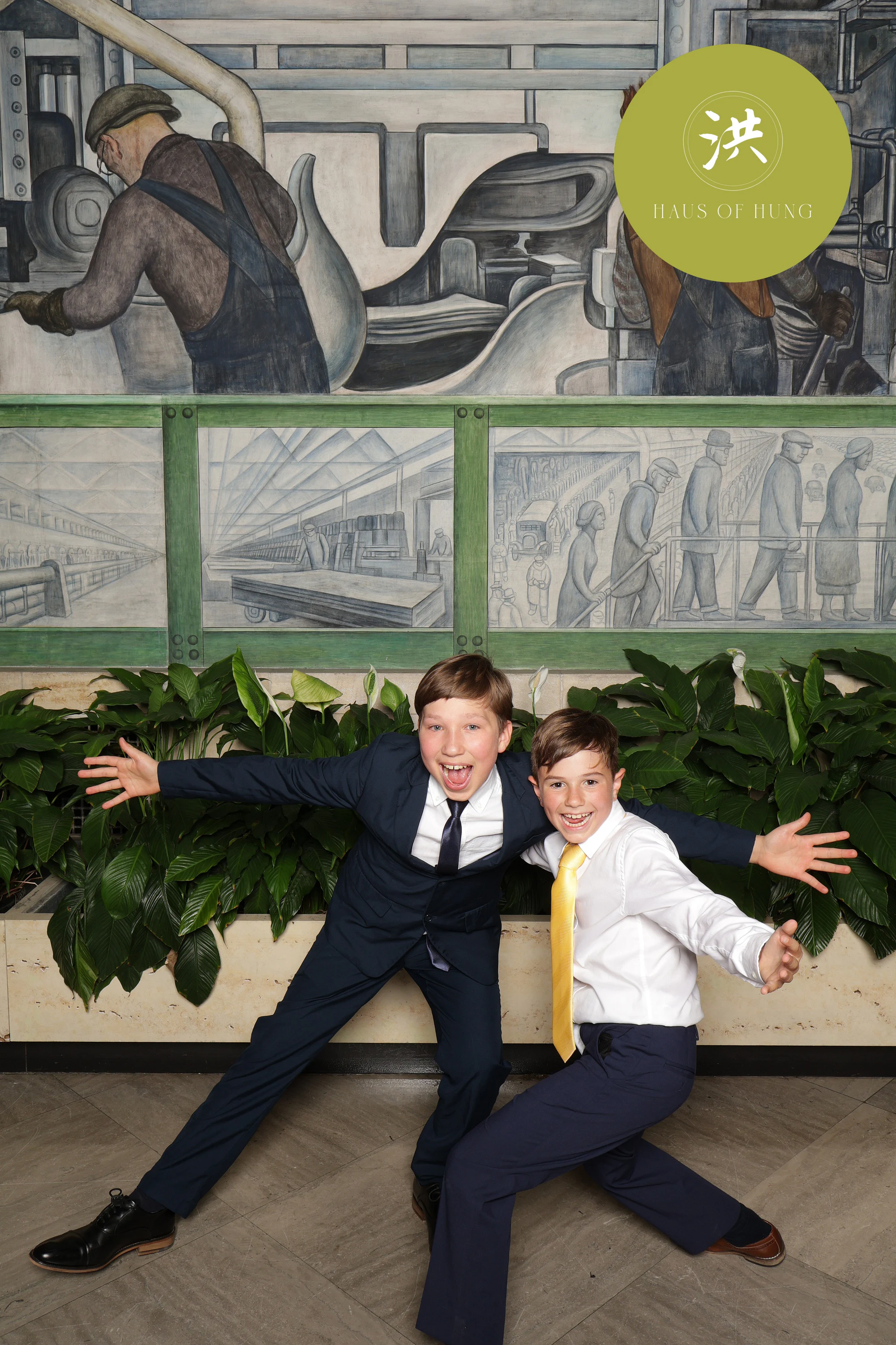 Two boys in suits with their arms thrown wide in front of the mural