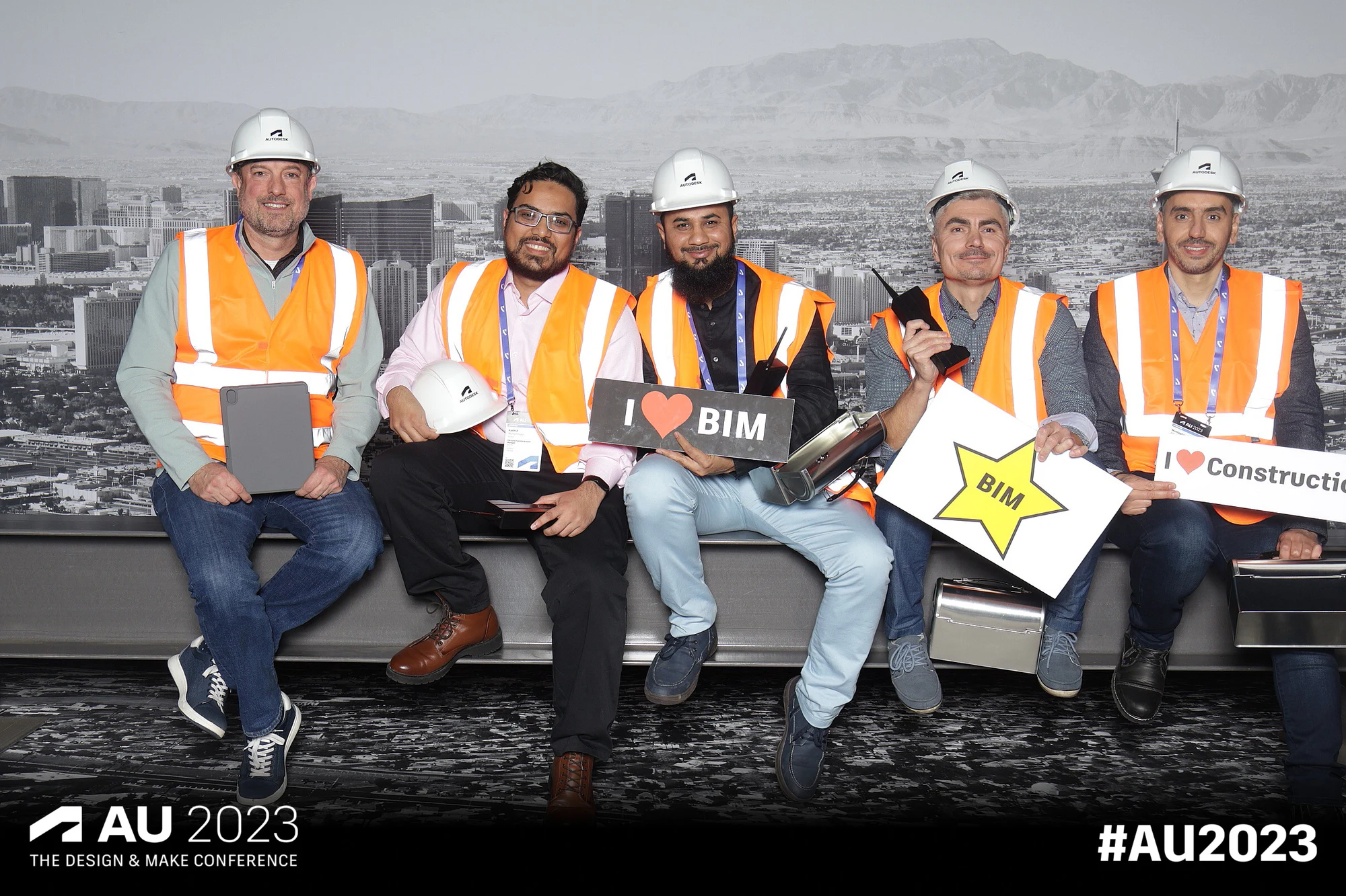 Five on the girder in hard hats with I love BIM and BIM star signs at Autodesk University 2023, the AU 2023 graphic along the bottom