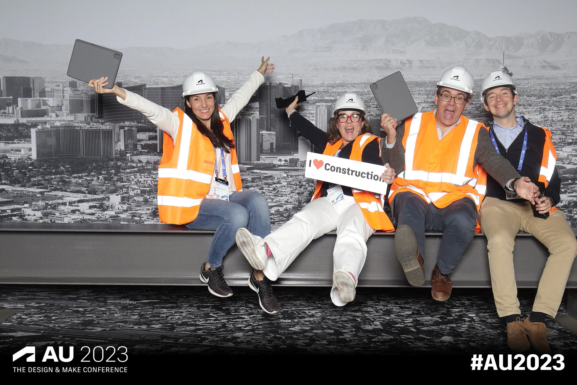 Four on the girder in hard hats, one with a sign and arms up, at Autodesk University 2023